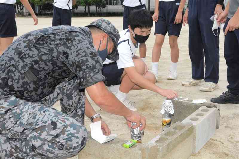自衛隊員の指導の下、空き缶を使って米を炊く生徒ら＝熊本市西区