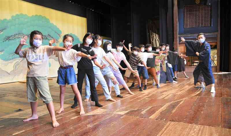 河合誠三郎さん（右）の指導の下、八千代座の舞台で歌舞伎の決めポーズ「見得」を切る子どもたち＝山鹿市