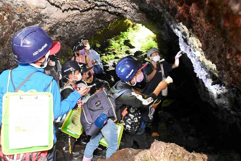 溶岩トンネルの一つ「米塚の穴」を見学する阿蘇西小の4年生ら＝阿蘇市