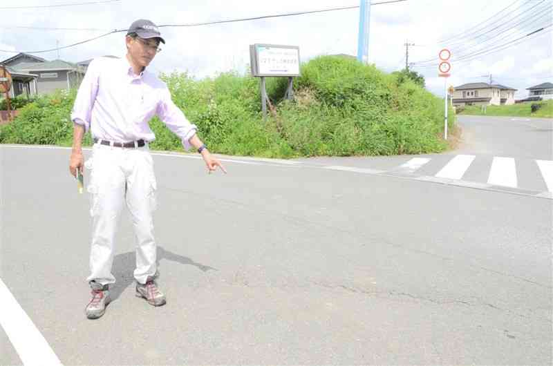 日奈久断層帯の北端部に位置する道路に熊本地震後に出現した亀裂を指差す遠田晋次教授。「6月の地震の影響は及んでいない」と話す＝14日、御船町