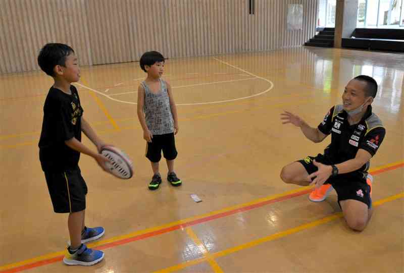 子どもたちにラグビーボールの投げ方を指導する西田雄吉さん（右）＝小国町
