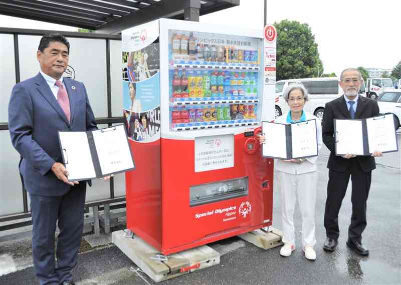 「スペシャルオリンピックス日本・熊本」を支援する飲料自販機の前で記念撮影する関係者ら＝益城町