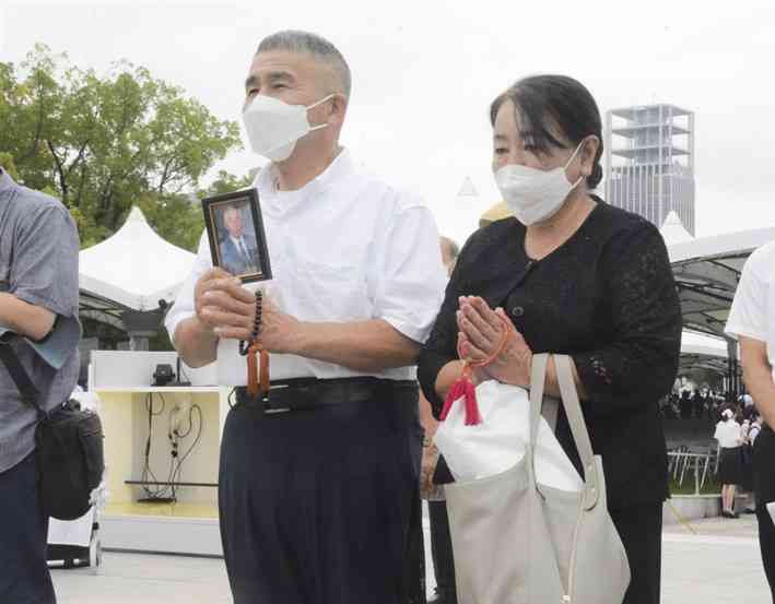 父堅夫さんの遺影を手に、原爆慰霊碑に手を合わせる菊川孝さん（左）と妻の美智子さん＝6日、広島市
