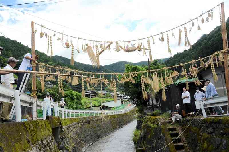 卵やタコなどのわら細工が中谷川の上空に揺れる七夕綱＝八代市