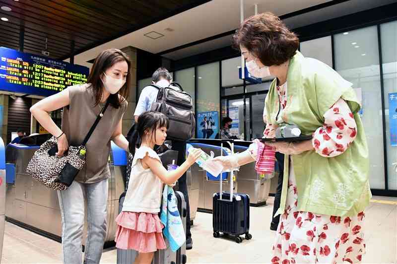 駅利用者にペットボトル入りの「熊本の水」を手渡す女将（右）＝10日、熊本市西区