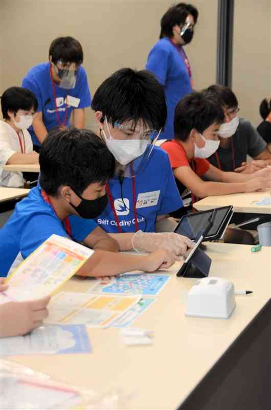 タブレットを使ってアプリ開発を体験する子どもとサポートする学生＝熊本市中央区