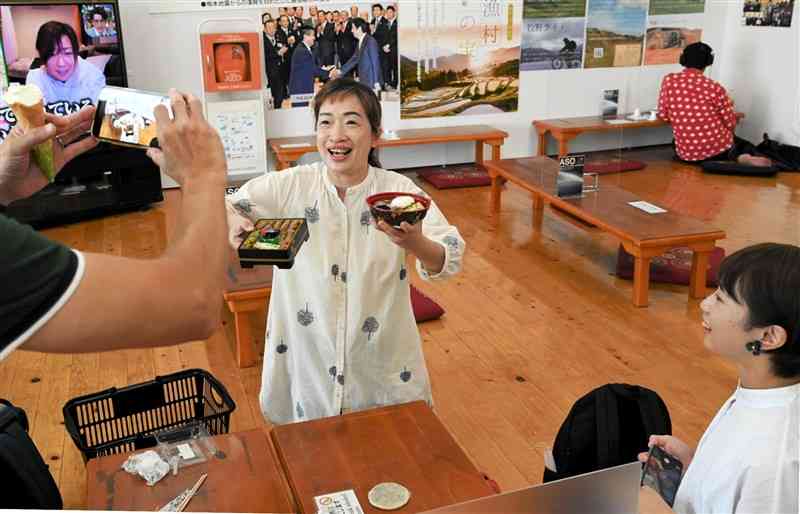 SNS用の動画撮影で道の駅阿蘇のあか牛丼を中国語でPRする阿金さん（中央）。右は前川空さん＝阿蘇市