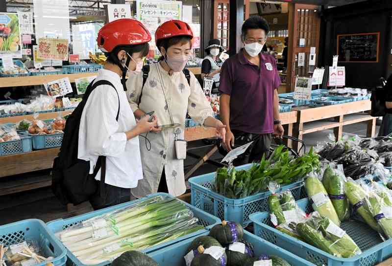 道の駅阿蘇で地元産の野菜を見学する阿金さん（中央）ら＝阿蘇市