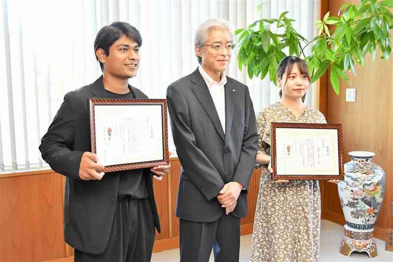 熊本信用金庫の井星伸一理事長（中央）から表彰状を受け取ったシャムスル・アバディ・ビン・ラムリさん（左）と夏野真衣さん＝熊本市中央区