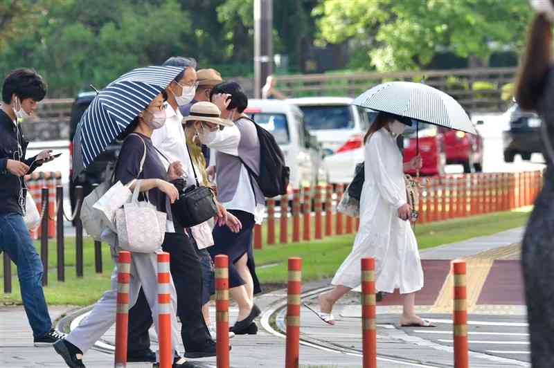 西日が残る中、日傘を差して歩く人ら＝15日午後4時ごろ、熊本市中央区の通町筋（谷川剛）