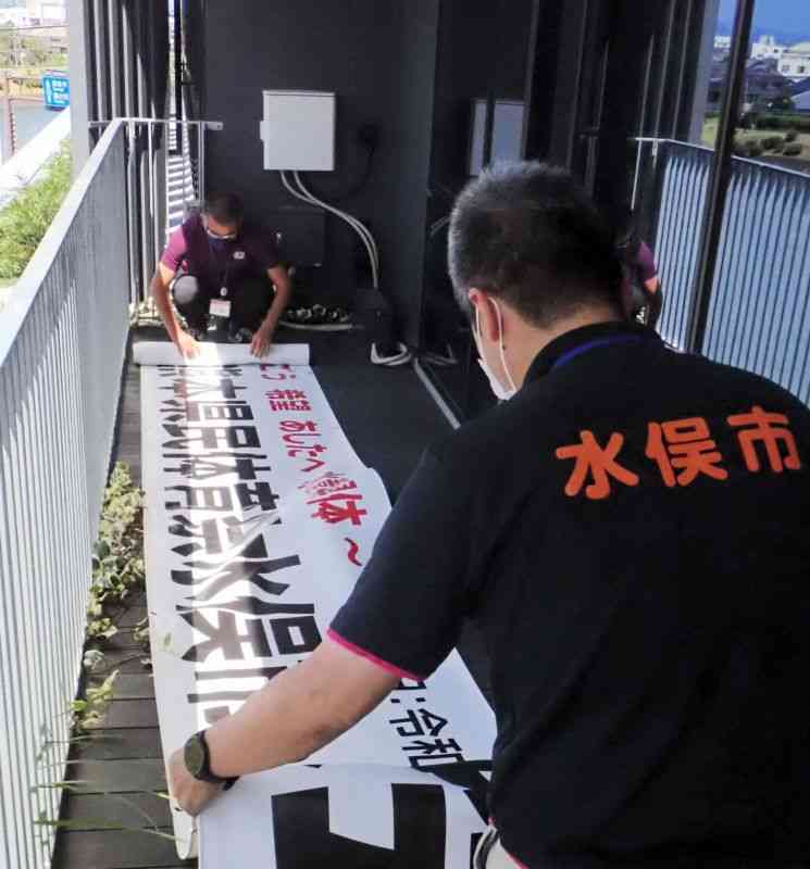 台風14号の接近で中止となった第77回県民体育祭の横断幕を片付ける水俣市職員＝16日、市役所