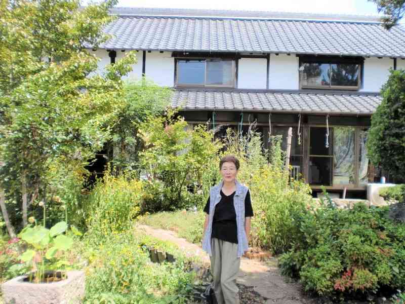 修復中の自宅古民家前に立つ城本真澄さん。「庭で育てた無農薬野菜で、お客さんをもてなしたい」と話します＝益城町