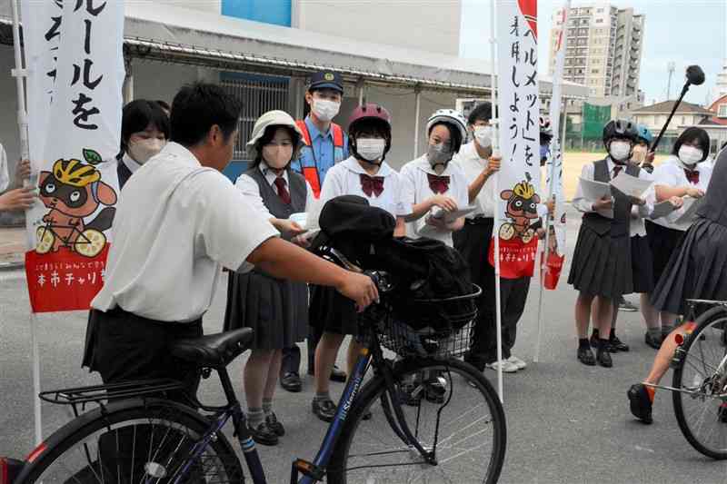 バリエーション豊富なヘルメットを実際にかぶってみせ、登校中の自転車通学生に着用を呼びかける鎮西高の生徒会役員ら＝9月22日、熊本市中央区