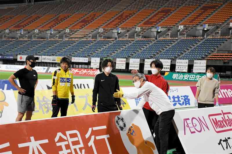 23日のリーグ最終戦に向けてスポンサーボードを設置するJ2ロアッソ熊本のスタッフとサポーターら＝22日夜、えがお健康スタジアム
