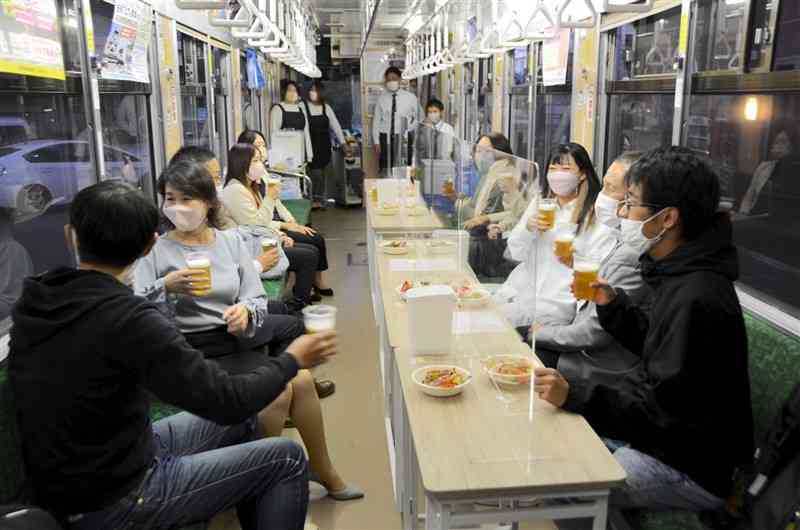 貸し切りの市電の車内で酒宴を楽しむ乗客ら＝熊本市中央区