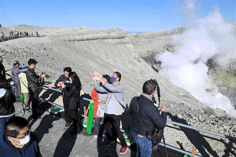 1年1カ月ぶりに見学ができるようになった中岳火口縁で、噴煙をバックに写真を撮る観光客ら＝9日午前9時15分ごろ、阿蘇市