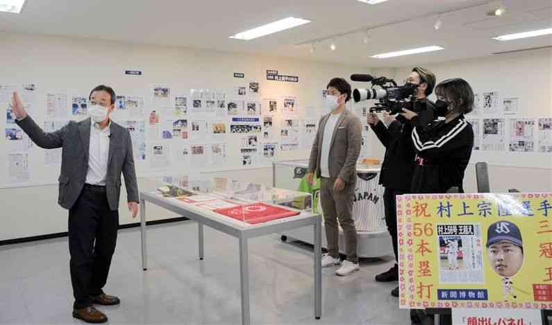 展示を説明する渡辺吉孝館長（左）を取材するヤクルト側のスタッフ＝熊本市中央区の新聞博物館