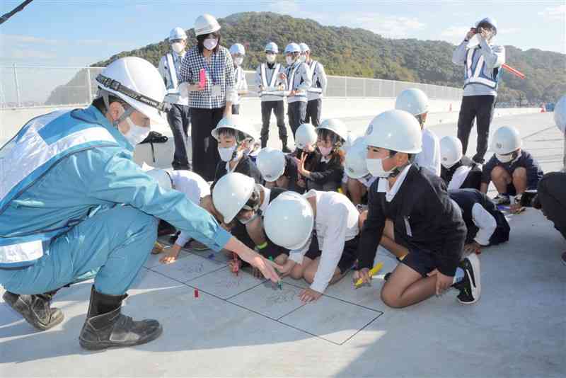 熊本西環状道路の工事現場を見学し、記念に手形を描く池上小の児童たち＝熊本市西区