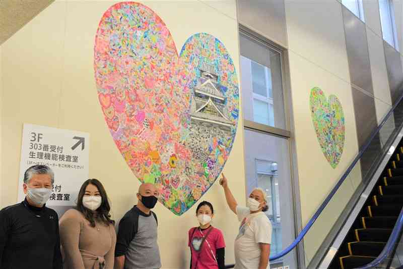 市民ら約500人が制作したハート形のホスピタルアート作品。デザインを監修した西村公一さん（右端）と、コミュナールの永廣佳理事（右から2人目）ら＝熊本大病院