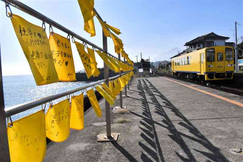 大三東駅のホームにはためく黄色いハンカチ。ホームに島原鉄道の黄色い列車が入ってきた。遠くには雲仙普賢岳がかすんで見える＝長崎県島原市有明町