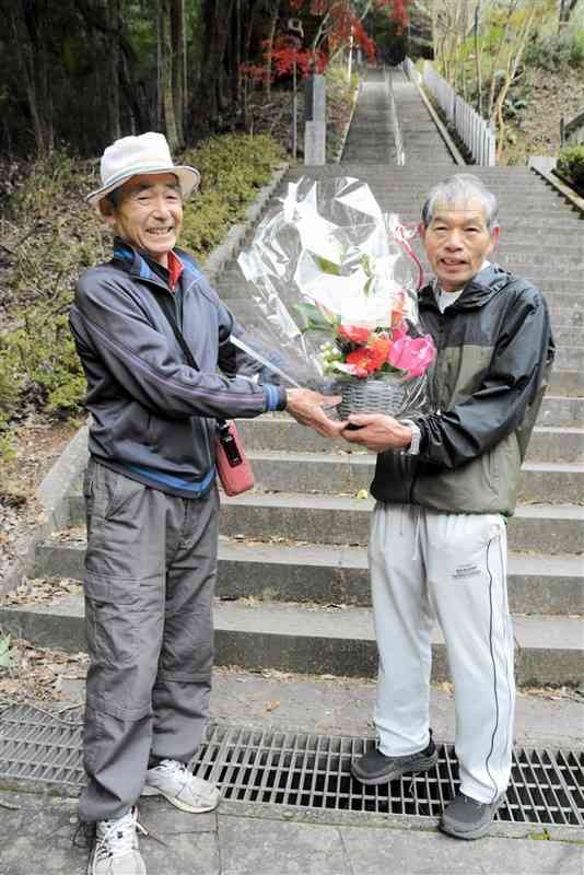石段往復1万5555回を達成した岩本靖成さん（右）とお祝いの花を贈る宮崎康喜さん＝美里町