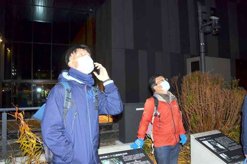 音声発生装置を使ったミヤマガラスの追い払いの効果を確認する佐賀大の徳田誠准教授（右）ら＝14日夜、熊本市中央区