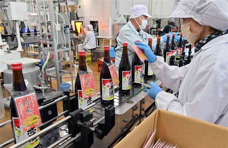 製造ラインを流れる赤酒に「屠蘇散」の袋を掛ける従業員＝19日、熊本市南区の瑞鷹