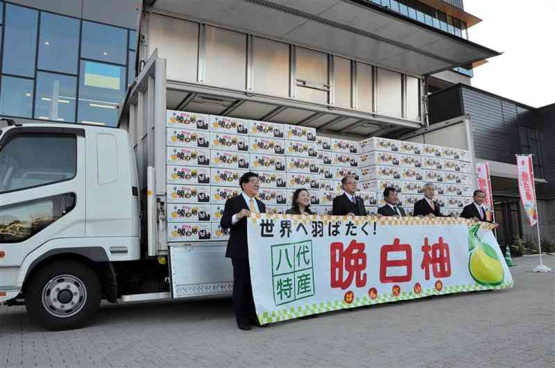 香港へ輸出するバンペイユが積み込まれたトラックの前で写真に納まる出発式の参加者＝八代市