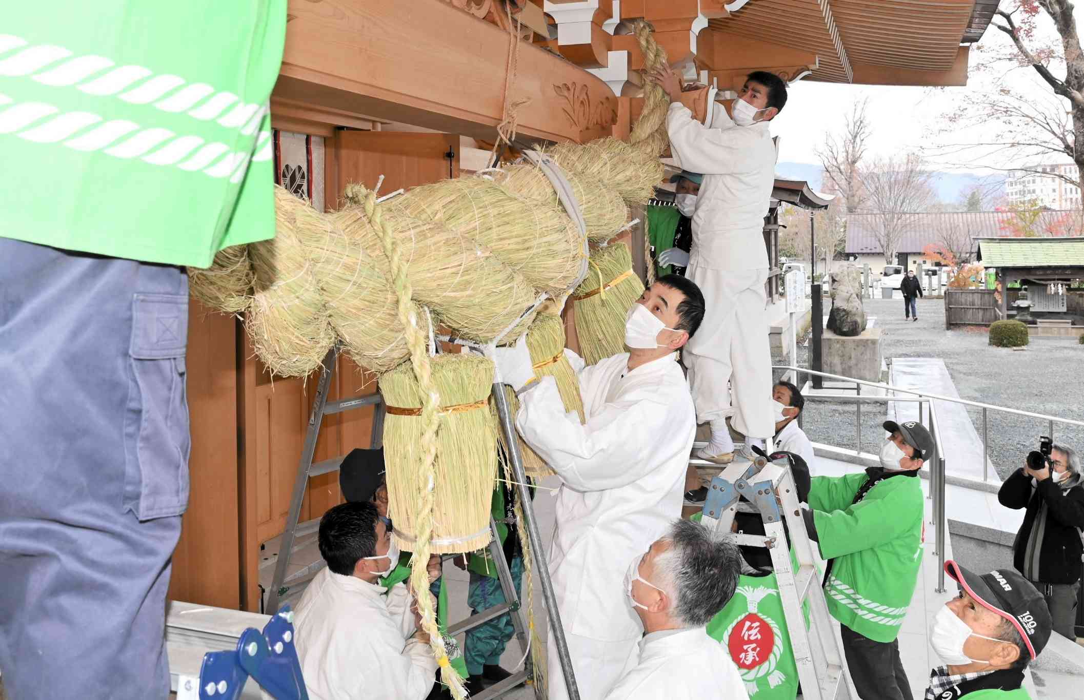 大しめ縄を拝殿に取り付ける阿蘇神社の神職や一の宮町大注連縄伝承会の会員ら＝12月7日、阿蘇市