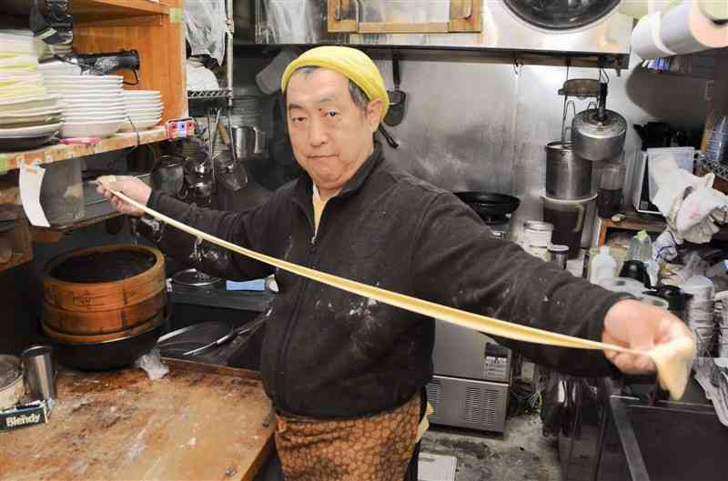 ビャンビャン麺を延ばす上村賢治さん。4メートルまで延ばして両端をつなげ、輪にするのが独特だ＝八代市