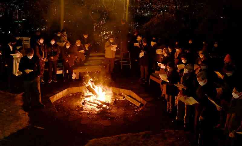 「熊本バンド」をしのぶ早天祈祷会で、たき火を囲み賛美歌を合唱する参加者＝30日午前6時30分ごろ、熊本市西区の花岡山（石本智）