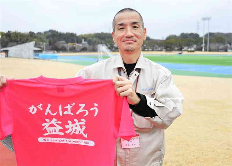 自身が復旧業務を担当した益城町総合運動公園で、熊本城マラソンで着用するシャツを手にする吉谷貴彦さん＝同町