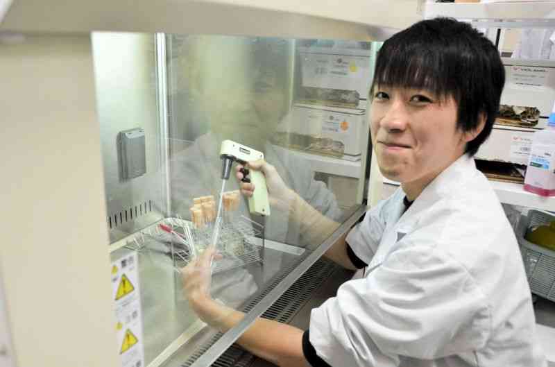 研究室で実験器具を手にする東海大大学院の中島勇貴さん＝熊本市東区