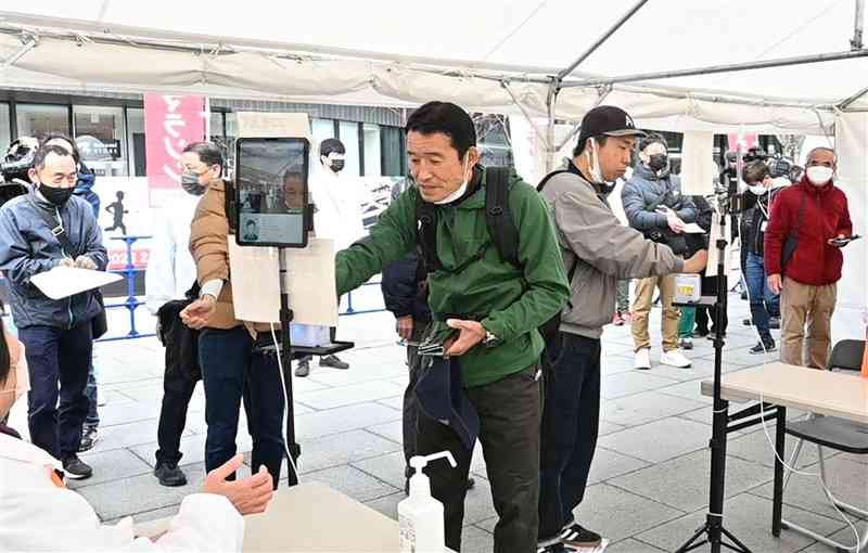 熊本城マラソンの出場受け付けが始まり、非接触の顔認証システムを使うランナーたち＝17日午前10時すぎ、熊本市中央区の花畑広場（谷川剛）