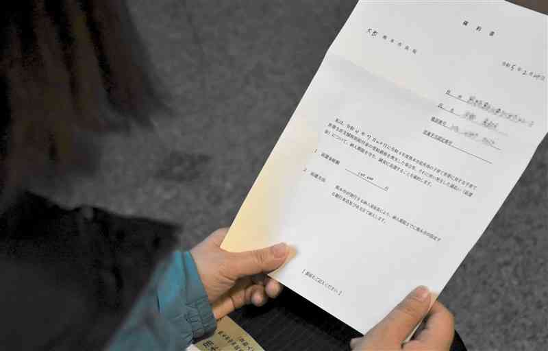 給付金の返還に先立ち、熊本市から提出を求められた「確約書」に目を落とす女性（写真の一部を加工しています）