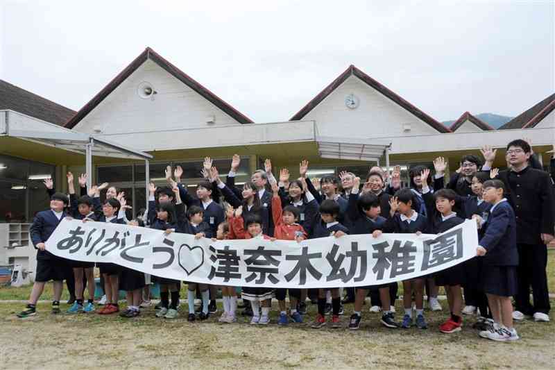 町立津奈木幼稚園の閉園式で横断幕を持って記念撮影する園児や小中学生ら＝津奈木町