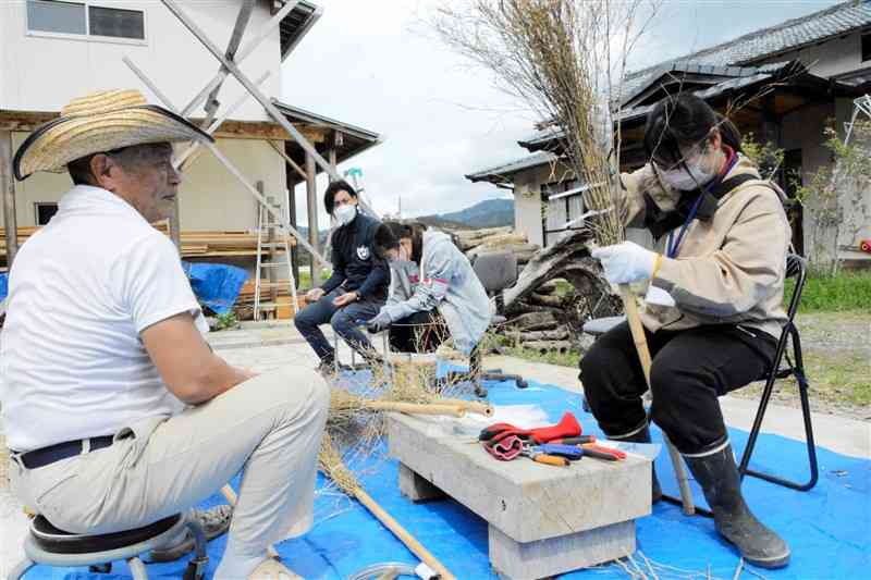 竹細工職人の大柿長幸さん（左）の指導を受け、竹ぼうき作りに励む九州看護福祉大の学生ら＝人吉市