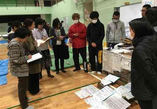 災害情報を英語で掲示したブース前で、打ち合わせをする学生や教職員ら＝２０１６年４月１８日、熊本市中央区の熊本大体育館（安部助教提供）