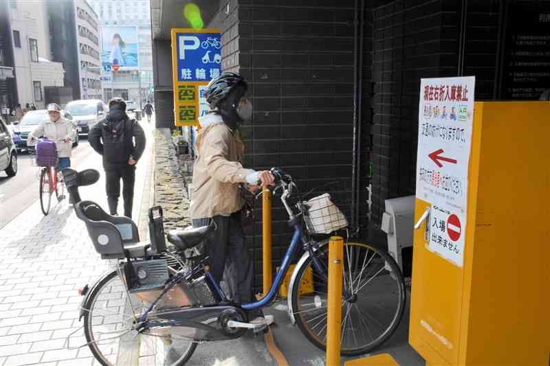 熊本市役所そばの駐輪場に入る、ヘルメットを着用した自転車利用者＝3月29日、同市中央区