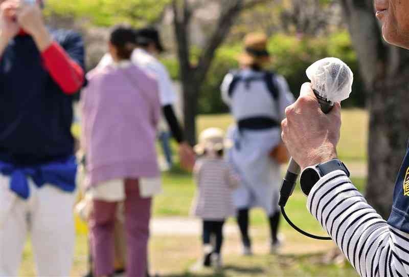 花見客が行き交う中、マスクを外しマイクで支持を訴える県議選の候補者＝2日午前11時ごろ、熊本市（鹿本成人）