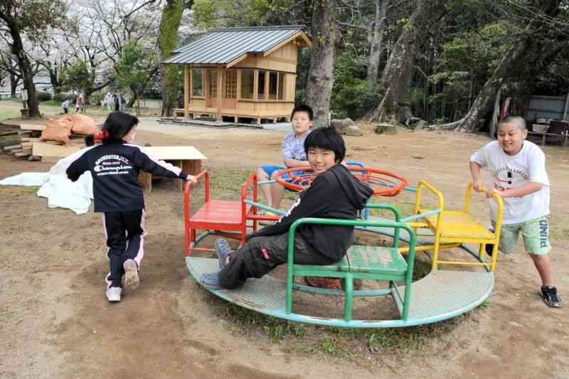 再建された龍王社（奥）が建つ公園で遊ぶ子どもたち。周囲は地震で被災し、新しく建て替えられた住宅や更地が目立つ＝3月30日、西原村