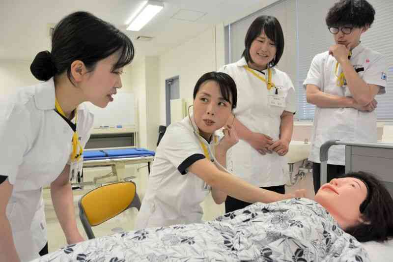 看護専門学校で学び、患者に見立てた人形に聴診器を当てる内山裕子さん（左から2人目）＝熊本市西区