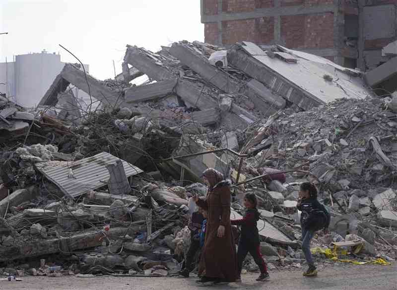 地震で大きな被害が出た（A）南部の町で、こわれた建物の前を通る子どもら＝2月（共同）