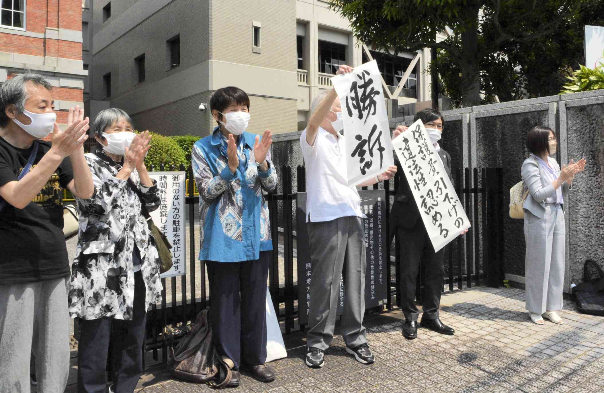 生活保護費の基準額引き下げは違法と認めた判決後、「勝訴」の垂れ幕を掲げて喜ぶ原告ら＝25日、熊本市中央区の熊本地裁前