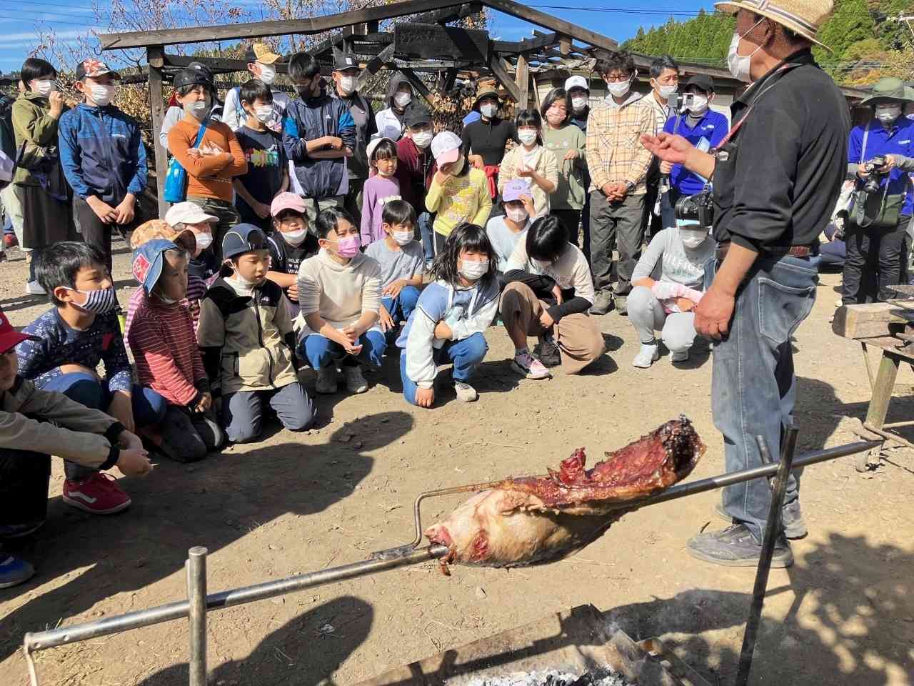 イノシシの塊肉を焼きながら、鳥獣被害についての甲斐村長の話を聞く子どもたち