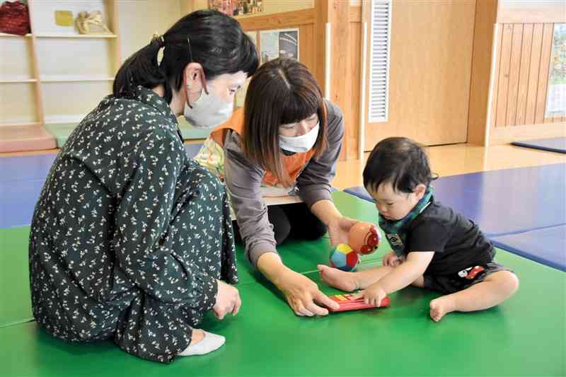 宮崎県三股町の子育て支援センターで子どもを見守る主婦（左）。「子育て環境の充実は移住の決め手の一つ」と話す