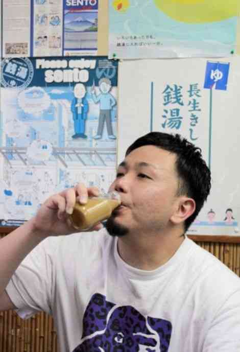 サウナを楽しんだ後、コーヒー牛乳を飲んでくつろぐ移住者の東拓郎さん＝4月下旬、熊本市中央区