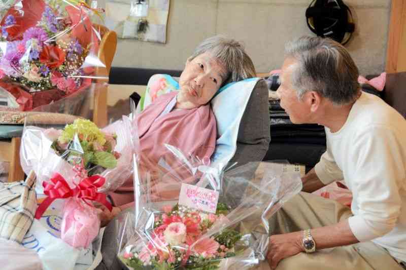 義兄の下田良雄さん（右）の問いかけに目を開けて応じる田中実子さん。70歳の誕生日を迎え、たくさんの花が届けられた＝3日、水俣市