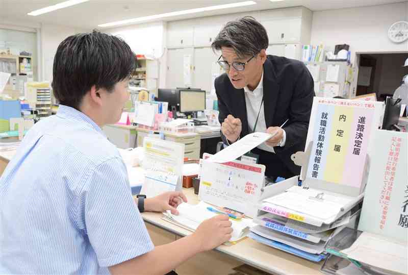 進路の報告に来た大学生（左）に書類手続きを説明する熊本学園大就職課の担当者＝6日、熊本市中央区