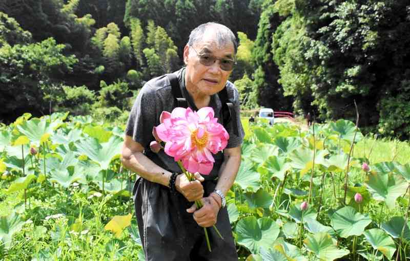 ハス園の前で花を持ち「多くの人に見に来てほしい」と話す竹下義雄さん＝和水町